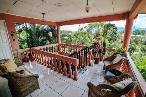 Upper covered terrace with wicker seating, toucan décor, and mountain views over the gardens.