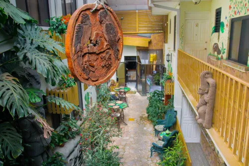 Garden walkway with a hand-carved macaw plaque, Monstera, and courtyard café tables.