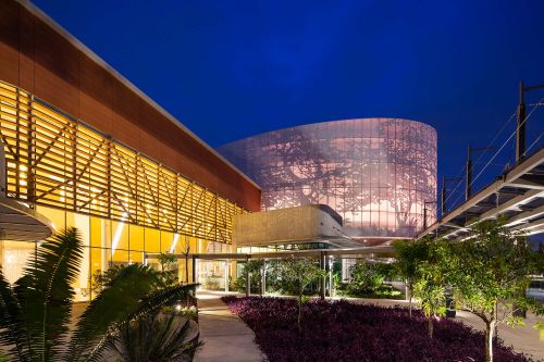 Modern exterior with wooden louvers and landscaped arrival plaza at twilight.